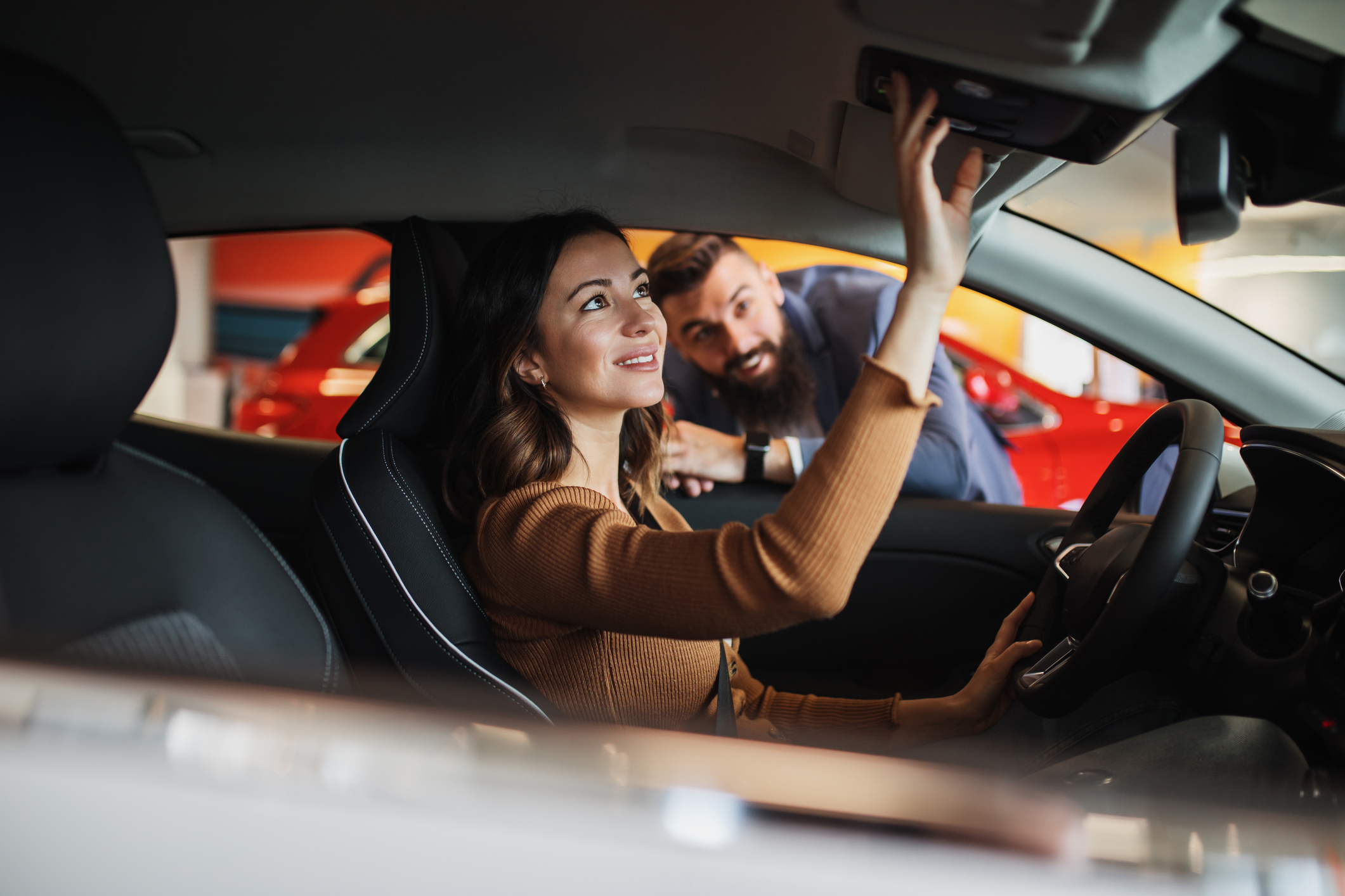 a women adjusting the rear view mirror of a car whilst at a car dealership